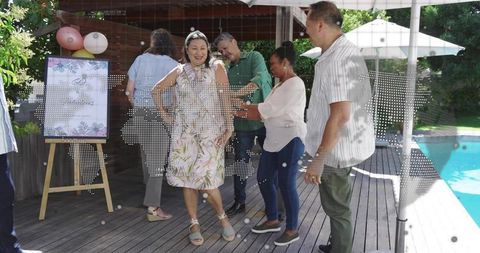 Middle-aged woman dancing with friends at backyard pool party on wooden deck celebrating