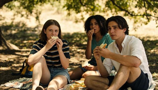 Young friends enjoying relaxed park picnic under trees sharing sandwiches and salad