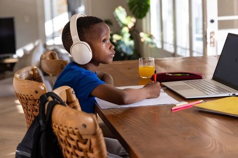 African american boy studying at home wearing headphones writing in notebook