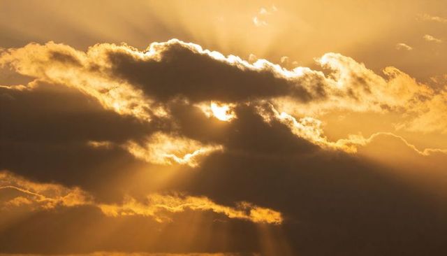Golden sunbeams breaking through dramatic cloudscape at sunrise with silver linings and rays