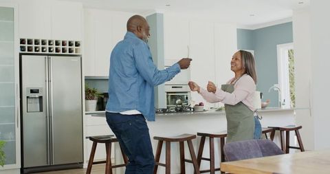Mature black couple dancing and cooking together in bright modern kitchen at island