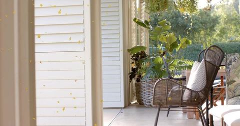 Sunlit wicker armchair with chevron pillow on patio surrounded by green plants and gold stars