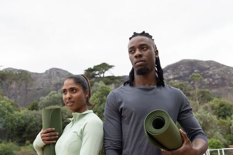 Diverse couple holding yoga mats on hillside trail preparing for outdoor workout