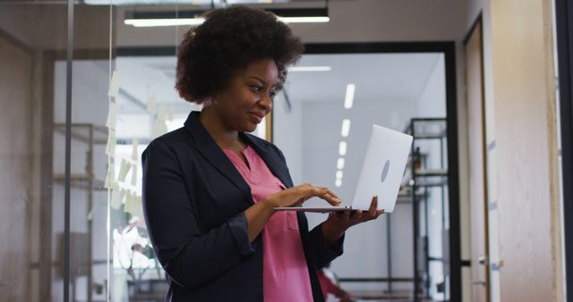 A businesswoman with an Afro hairstyle using a laptop in a modern office environment. Suitable for depicting professional life, corporate settings, technology usage, and workplace productivity.