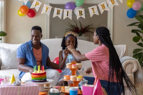 African american family celebrating daughter birthday at home with rainbow cake, balloons, cupcakes