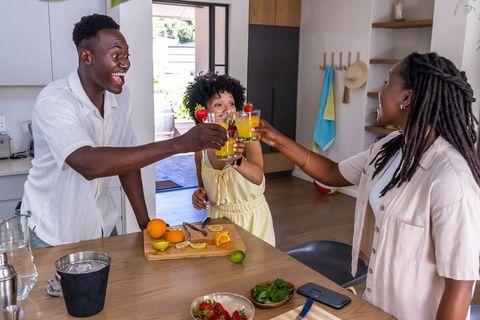 African american family toasting with fresh orange juice at modern kitchen island morning