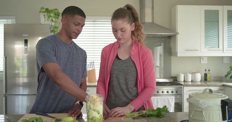 Young diverse couple preparing green smoothie together on kitchen island in modern home