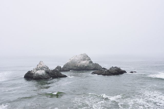 Depicts isolated rocky islets surrounded by misty ocean and gentle waves on a foggy day. Suitable for promoting travel to coastal regions, inspiration for tranquility and nature retreats, or as relaxing background.