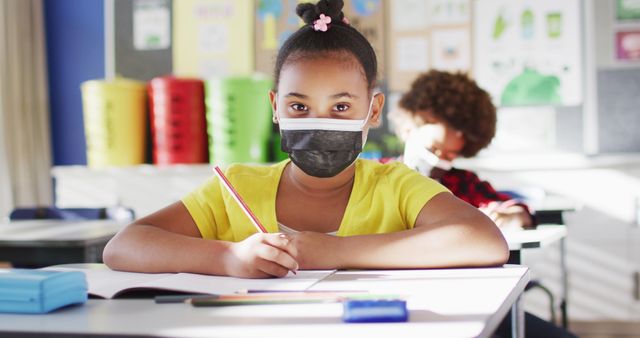 Portrait of biracial schoolgirl wearing face mask in classroom looking at camera - Download Free Stock Photos Pikwizard.com