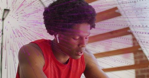 Young man catching breath after intense home workout wearing earbuds and red tank top
