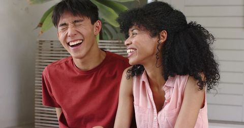 Young diverse couple laughing together on indoor bench, casual cozy lifestyle moment
