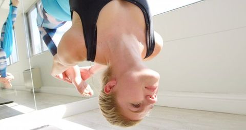 Woman hanging in aerial yoga inversion with teal hammock and mirror reflection sunlight