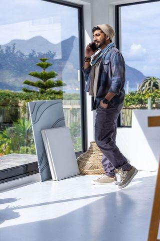 Creative man talking on phone in sunlit minimalist studio with mountain and garden views