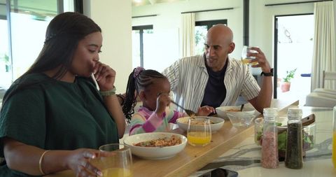 Multicultural family enjoying relaxed breakfast at sunlit kitchen bar with orange juice