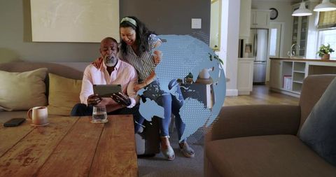 Mature couple exploring digital globe on tablet in cozy open-plan living room