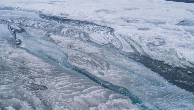 Aerial glacier surface revealing turquoise meltwater channels and layered crevasses