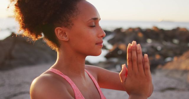 African woman practicing meditation near ocean at sunset. Ideal for fitness, wellness, mental health, and mindfulness content. Promotes tranquility, stress relief, and connection to nature. Suitable for articles, blogs, and advertisements related to mental well-being, outdoor activities, and yoga practices.