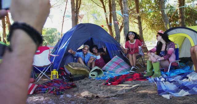 Friends relaxing during a summer camping trip in the forest. They are sitting around tents, posing for a photograph, smiling and having fun. This scene can be used for promoting outdoor activities, travel, friendship, vacation, and holiday adventures.