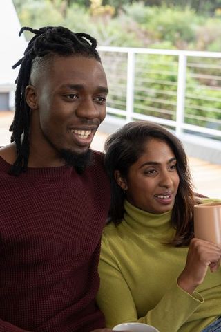 African american man and indian woman relaxing on terrace holding mugs cozy couple