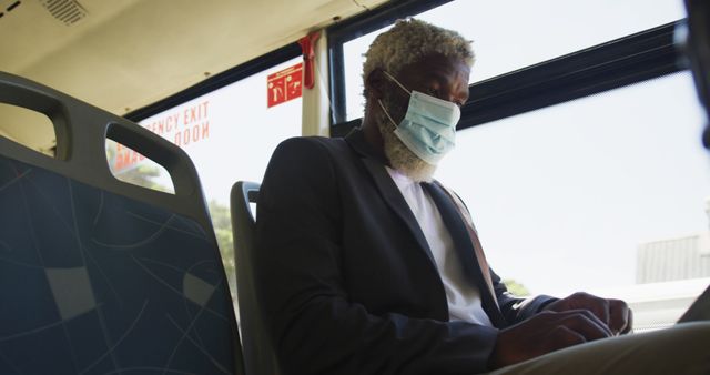 African american senior man wearing face mask using laptop while sitting in the bus. hygiene and social distancing during coronavirus covid-19 pandemic.