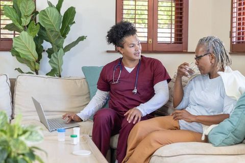 Home nurse consulting senior african american woman taking medication while using laptop