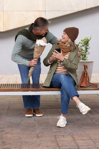 Senior couple sharing flowers and laughter on bench in urban plaza