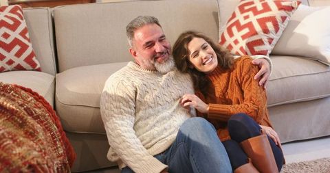 Cozy Couple Relaxing on Living Room Floor Wearing Knit Sweaters, Smiling and Cuddling