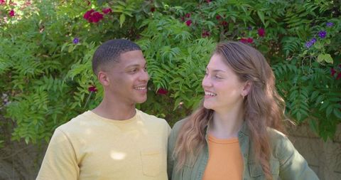 Young diverse couple smiling and sharing moment in sunlit garden with magenta blooms