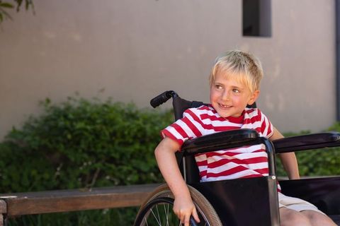 Smiling blond boy in wheelchair outdoor courtyard, accessible mobility and inclusion