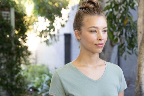 Serene young woman standing in sunlit courtyard wearing light green v-neck tee