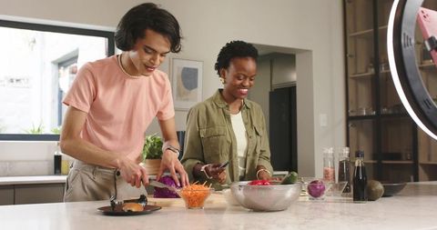 Couple chopping fresh vegetables together in modern kitchen, filming cooking content