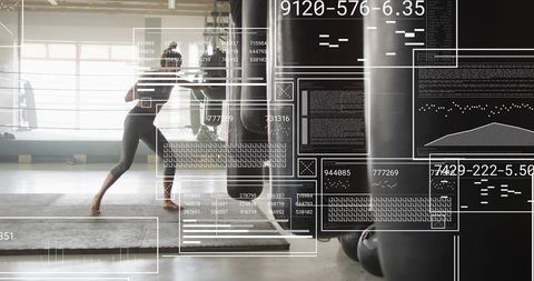Striking woman hitting heavy bag in sunlit gym with futuristic hud fitness data overlay