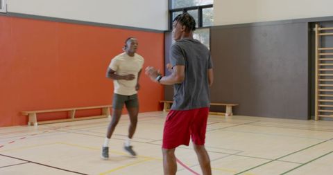 Asian player dribbling while teammate defending during indoor basketball training session
