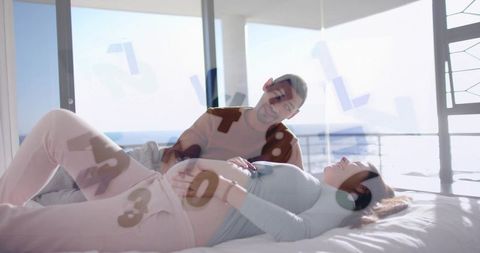 Pregnant woman and partner sharing serene seaside maternity moment on bed with ocean view