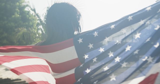Woman holding an American flag outdoors on a bright sunny day. Ideal for usage in patriotic themes, USA Independence Day celebrations, July 4th events, and expressions of national pride and freedom.