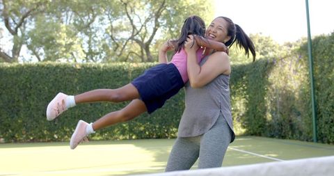 Mother Joyfully Lifts Daughter on Tennis Court Outdoors