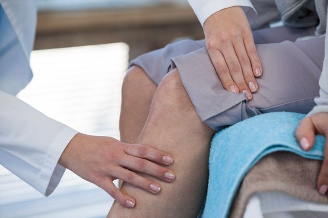 Doctor examining patient's knee in a clinical setting. Useful for illustrating medical checkups, healthcare services, physical therapy, and injury assessments. Ideal for medical websites, healthcare brochures, and educational materials.