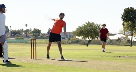 Indian man fast bowling on cricket pitch with batter and fielder during sunny park match