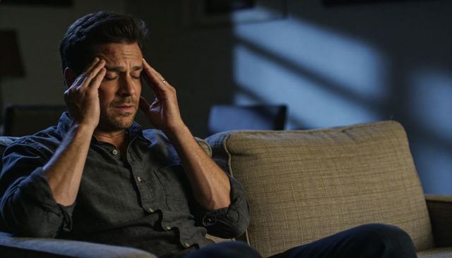 Stressed man rubbing temples on couch at night showing headache, fatigue and solitude