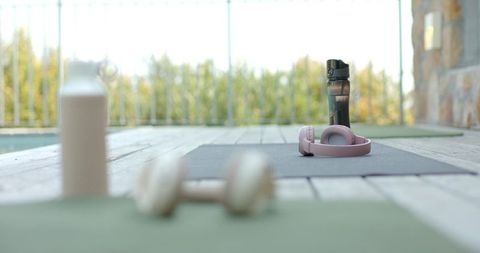 Pink headphones resting on yoga mat with water bottle on outdoor wooden deck for workout