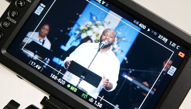 Bearded male vocalist singing on stage viewed through camera monitor during worship