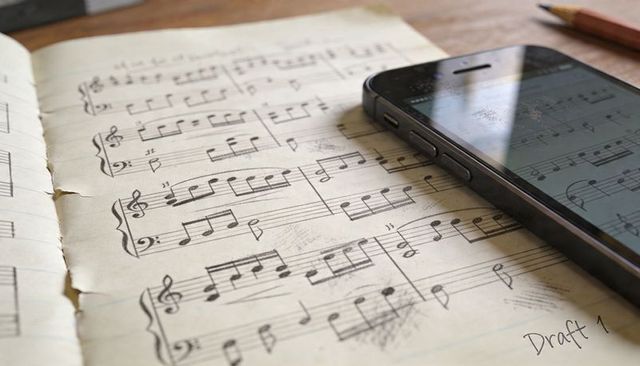 Vintage sheet music draft with smartphone and pencil on wooden desk, closeup handwritten notes