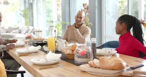 Multigenerational diverse family sharing sunlit brunch at wooden dining table with fresh bread