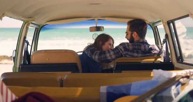 Couple sharing a moment of affection while sitting in the back of a van parked at a beach with a scenic ocean view. Perfect for themes related to travel, romantic getaways, summer adventures, and road trips.
