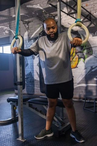 African american man gripping gym rings training in industrial urban gym with graffiti