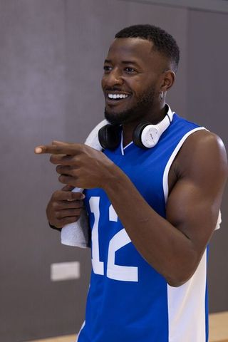 Smiling athlete wearing headphones pointing while holding towel, blue number 12 sports jersey