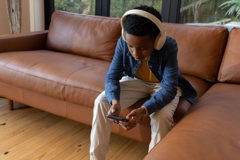 African american boy listening to music using smartphone while sitting on leather sofa