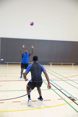 African american men practicing volleyball in indoor gym wearing matching blue uniforms