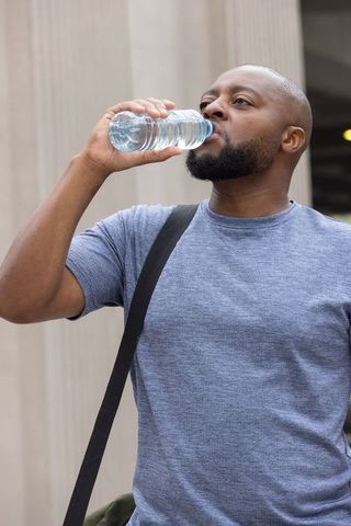 African american man drinking water while commuting near urban column architecture