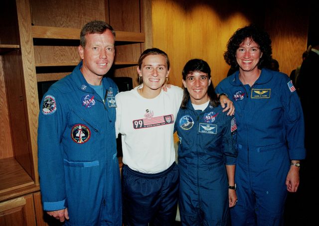U.S. Women's World Cup soccer team member poses with NASA astronauts Paige Laurie, Steven W. Lindsey, Nancy Jane Currie, and Laurel B. Clark at Cape Canaveral Air Station. This moment marks a convergence of sports and space exploration as the team visited to watch Space Shuttle mission STS-93, commanded by the first female commander Eileen M. Collins. The launch, carrying the Chandra X-ray Observatory, marked a significant milestone for women in STEM. Great for use in articles celebrating achievements of women, STEM promotion, and historical events in space exploration.